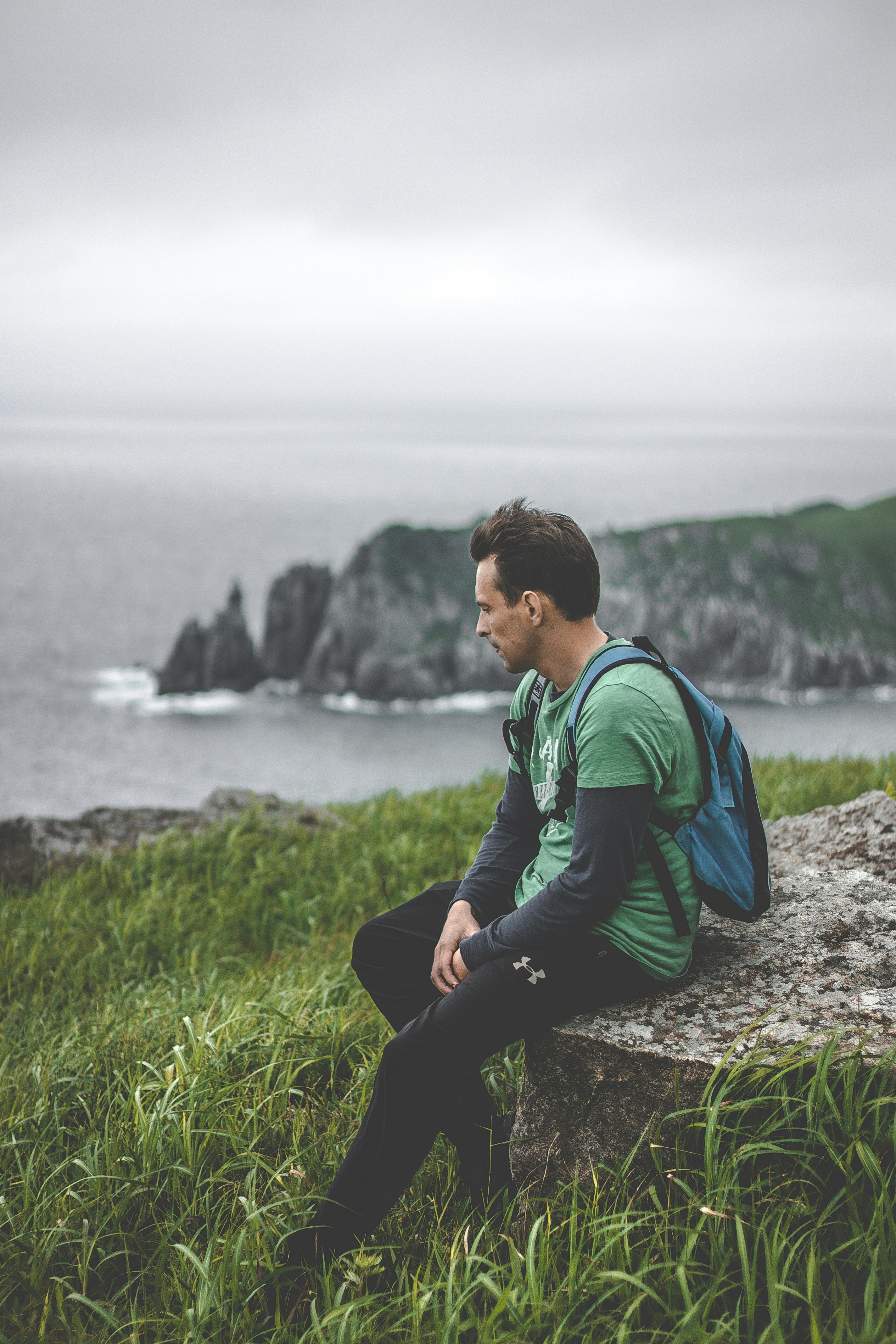 man sitting on gray rock with green grass